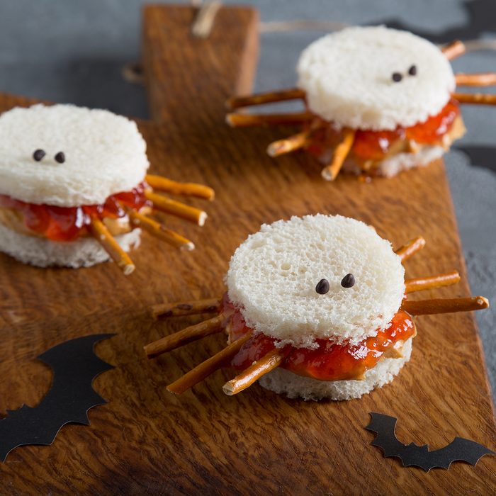 Spooky peanut butter and jelly spider sandwiches with paper bats for halloween on a brown rustic cutting board.