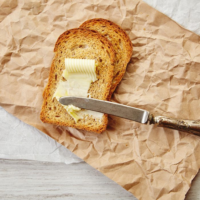 Top view of two slices of rye dry bread as toast with butter for breakfast with vintage knife on it. Everything on craft paper.