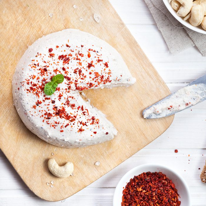 Vegan raw cheese from cashew nuts spread on the bread by knife on the white wooden background