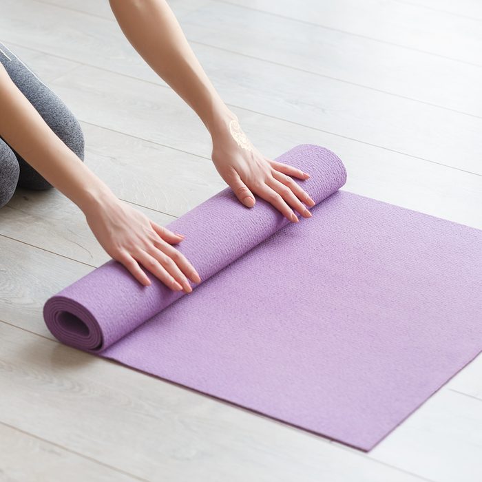 Young yoga Woman rolling her lilac mat after a yoga class on wooden floor near a window
