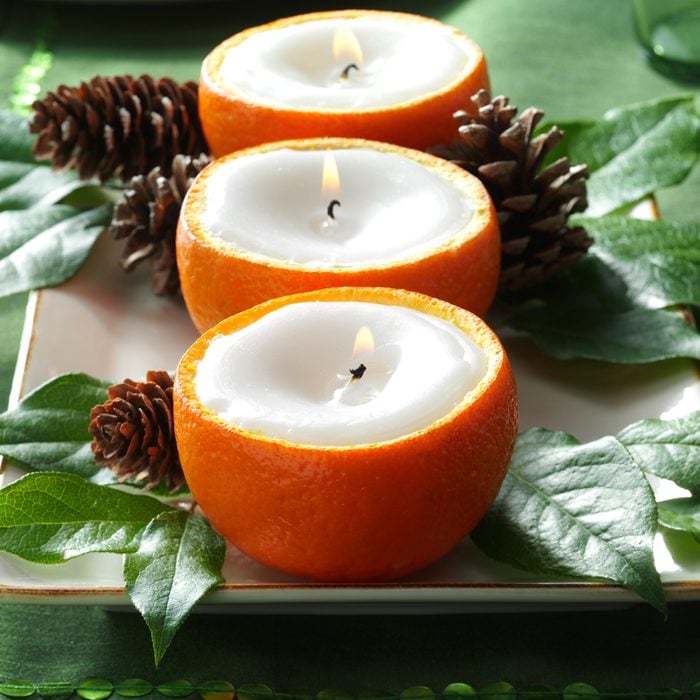 Citrus Candles Displayed on a Forest Green tablesetting with various leaves and pine cones scattered around the display