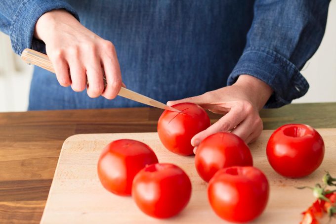 woman scoring skin of tomato on wooden cutting board