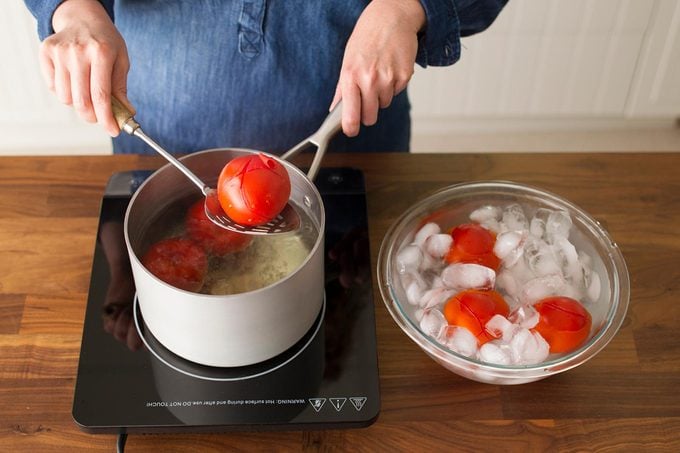 woman placing tomato in ice bath from boiling pot