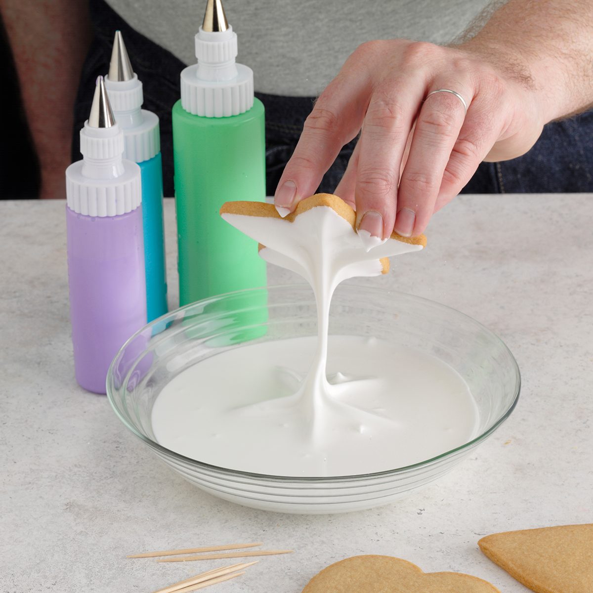 A person dipping cutout cookies into a bowl of royal icing.