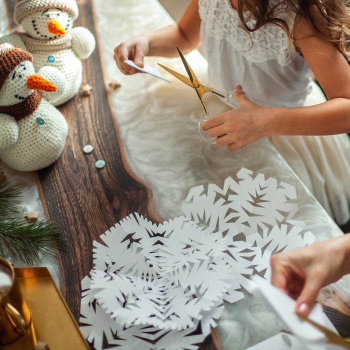 Little Cute Girl And Young Beautiful Woman Cut Snowflakes From White Paper with felt snowmen and hot cocoa in the background of the craft scene