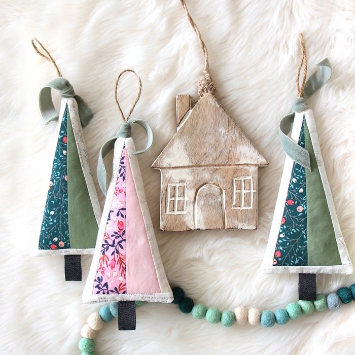 Quilted Ornaments Shaped Like Christmas Trees and Houses Rest against a White Fur Background with a Felt Garland Entering and Exiting the lower part of the Frame