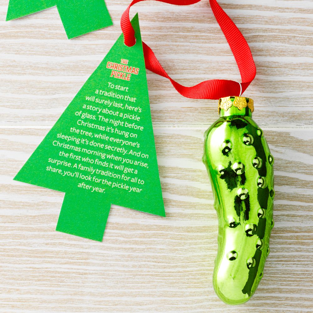 The Christmas Pickle, a Glass Pickle Ornament, pictured with a cutout of a Christmas Tree with Instructions on how to follow the silly Christmas Tradition