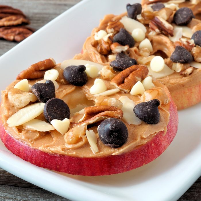 Autumn apple rounds with peanut butter, chocolate chips and nuts, on white serving plate