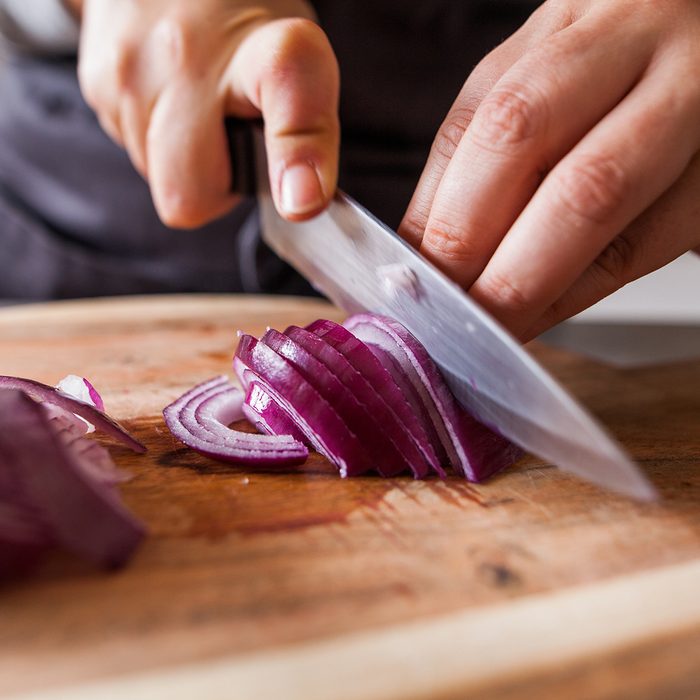 Cette photo représente une personne en train de couper des oignons rouges dans une cuisine.