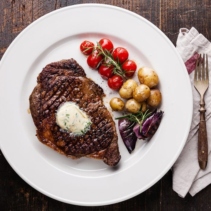 Grilled steak Ribeye with herb butter and baby potatoes on white plate on wooden background