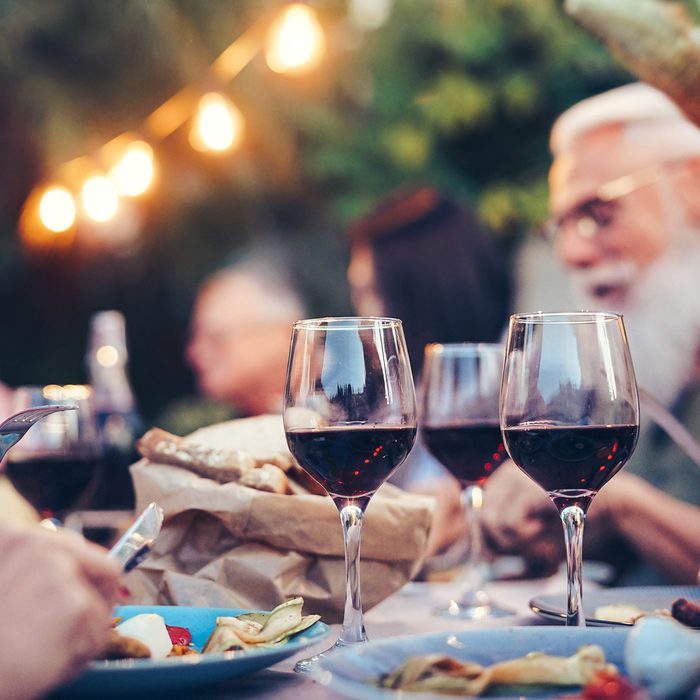 Happy family eating and drinking red wine at dinner barbecue party outdoor - Mature and young people dining together on rooftop - Youth and elderly weekend lifestyle activities - Focus on wineglass