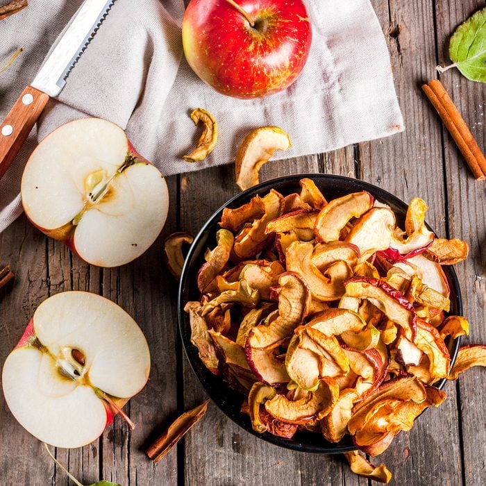 Homemade sun-dried organic apple slices, crispy apple chips, on an old rustic wooden table with fresh apple and cinnamon. Copy space top view