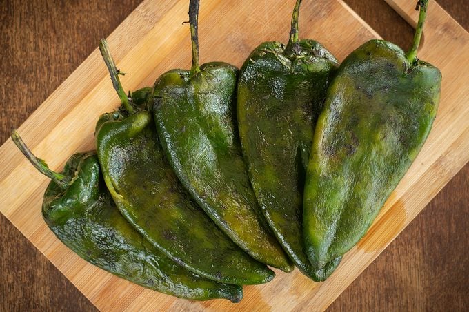 This image portrays 5 Poblano peppers roasted and deskinned, laid over a cutting board. This chili originates from Puebla, Mexico, and is typically used this way for recipes likes Chiles Rellenos (stuffed peppers) or Chiles en Nogada (Stuffed peppers drenched in walnut-based sauce). They are a common sight in Mexican households and a cultural staple in the country's culinary roots.
