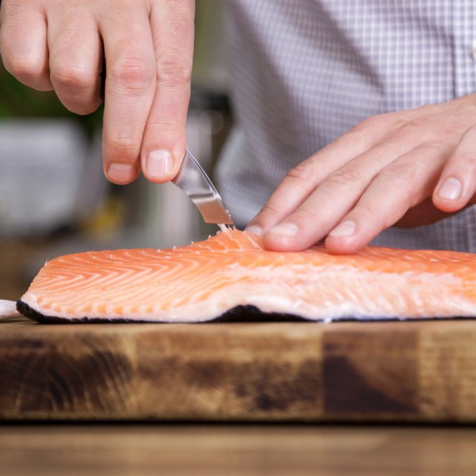 Close up of man removing fish bone out from salmon and preparing food in the kitchen.