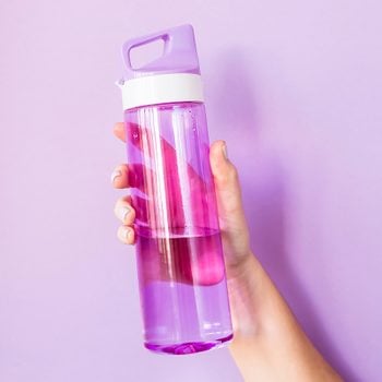 A woman holds a purple water bottle in her hand for sports. On a bright purple background. Healthy lifestyle and fitness concept; Shutterstock ID 1055321852; Job (TFH, TOH, RD, BNB, CWM, CM): Taste of Home