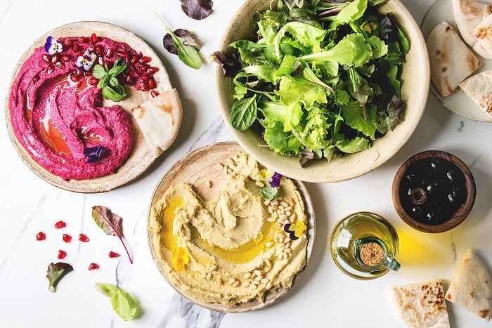 Variety of homemade traditional and beetroot spread hummus with pine nuts, olive oil, pomegranate served on ceramic plates with pita bread and green salad on white marble background. Flat lay, space.; Shutterstock ID 1120310000; Job (TFH, TOH, RD, BNB, CWM, CM): Taste of Home