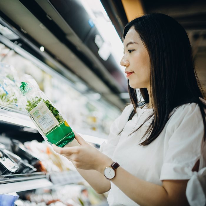 Young Asian woman with cart grocery shopping for fresh produce. She is shopping for fresh vegetables in a supermarket