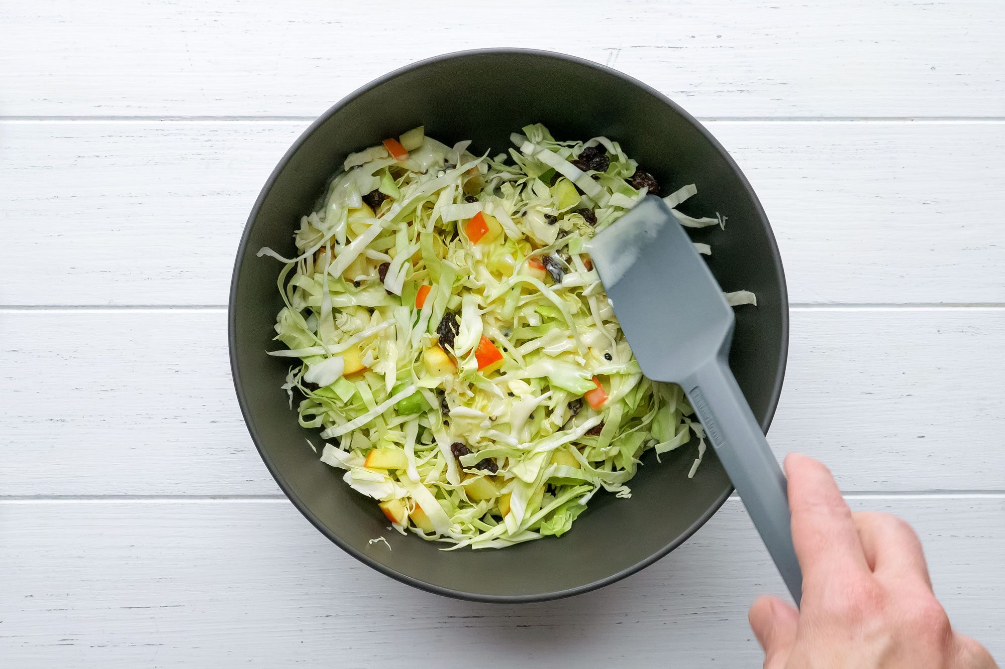 Tossing Apple Slaw Mix in a large bowl on painted wooden surface