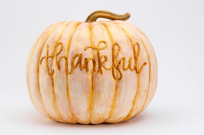 rustic light orange and white painted pumpkin with the word "thankful"