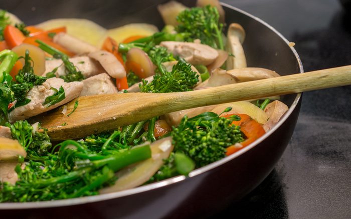 Close-up and side view of wooden spoon stirring chicken and vegetables in cast iron skillet
