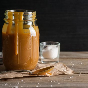 Homemade salted caramel sauce, in a jar, with a spoon.
