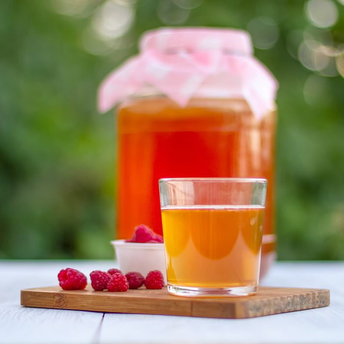 Glass jar with Kombucha, poured glass with Kombucha and raspberries in the summer garden.