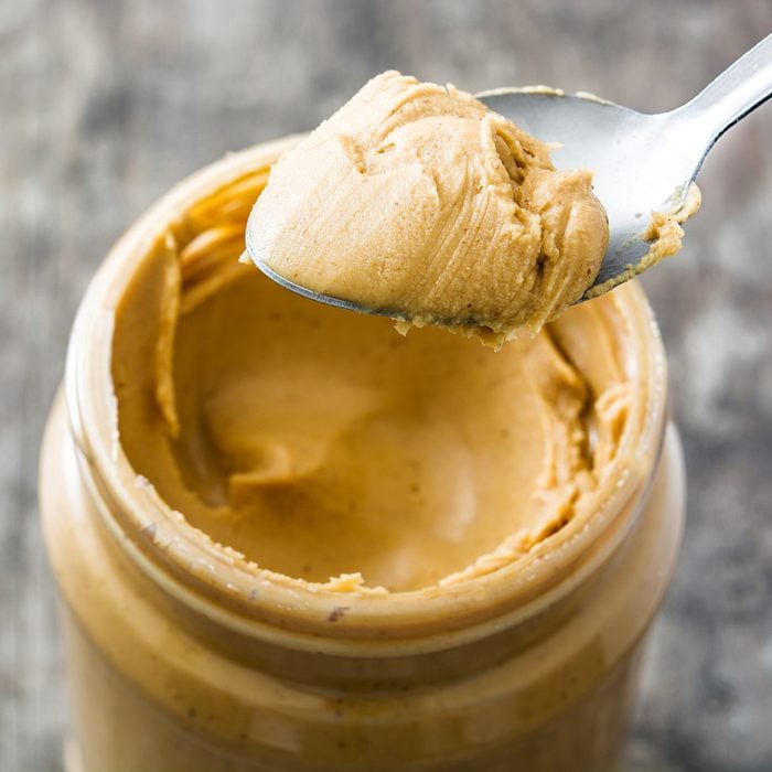 Creamy peanut butter and spoon on wooden background