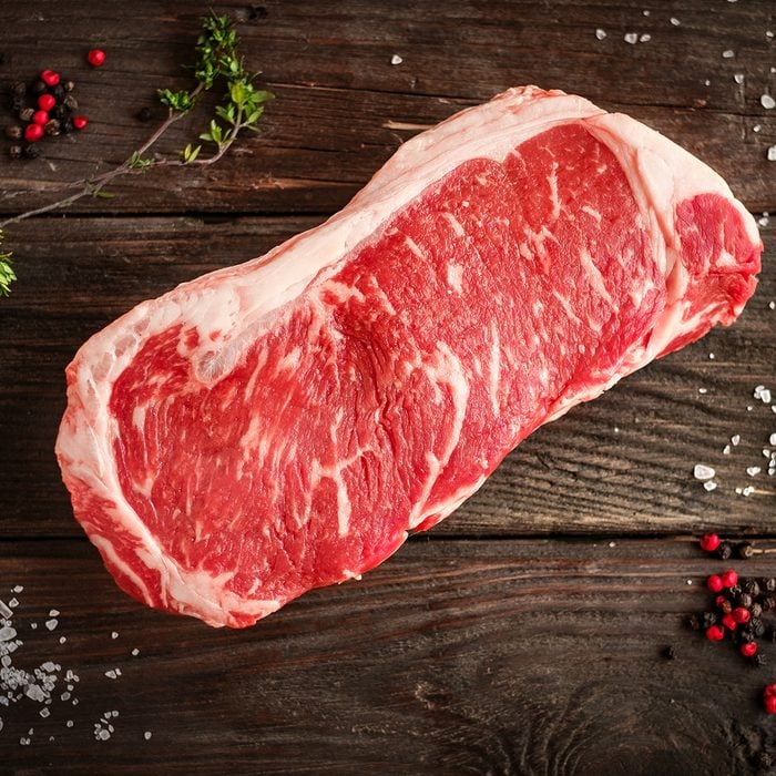 raw strip loin steak on white wooden background in rustic style with salt and herbs