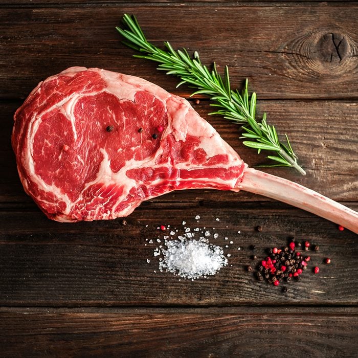 raw Tomahawk steak on wooden background with spices for grilling