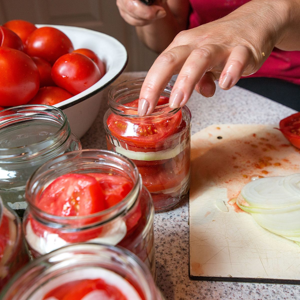 Canning fresh tomatoes with onions in jelly marinade. Woman hands putting red ripe tomato slices and onion rings in jars. Basil, parsley leaves on top of onions. Vegetable salads for winter ; Shutterstock ID 1205461483; Job (TFH, TOH, RD, BNB, CWM, CM): TOH