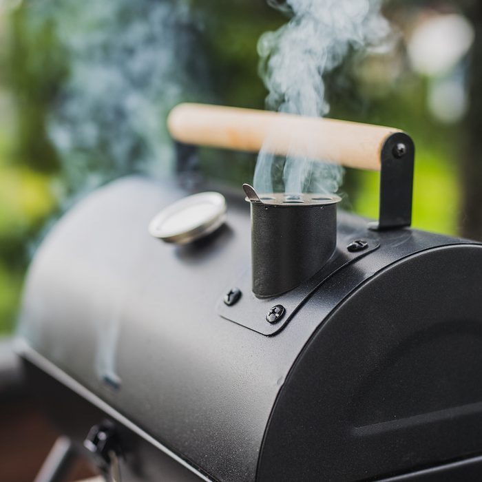 Smoke coming out of a smokestack of a small black smoker grill or barbecue on green background.; Shutterstock ID 1408814591; Job (TFH, TOH, RD, BNB, CWM, CM): TOH