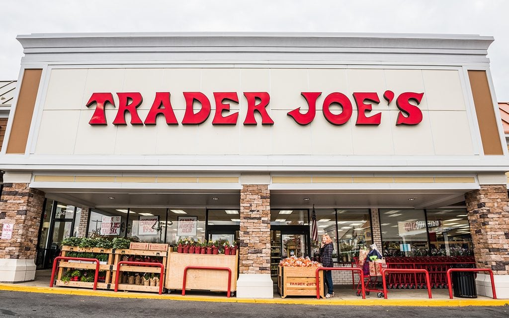 Trader Joes grocery store facade with sign and items on display and people walking
