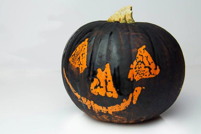 black pumpkin with an orange face using a Wax Resist Painting method