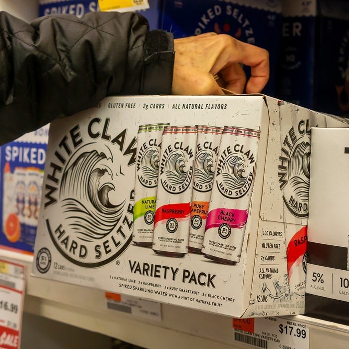 A discerning consumer chooses a case of White Claw brand hard seltzer among other brands in a cooler in a supermarket