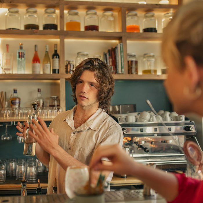 Young male bartender holding a bottle while standing behind the counter of a trendy bar taking drink orders from customers