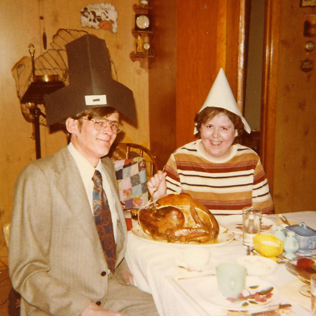 two older siblings wear funny pilgrim hats at the dinner table