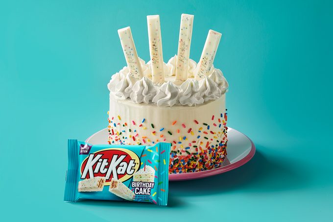 birthday cake kit kat package in front of a beautiful birthday cake decorated with some birthday cake kit kat bars; on aqua background