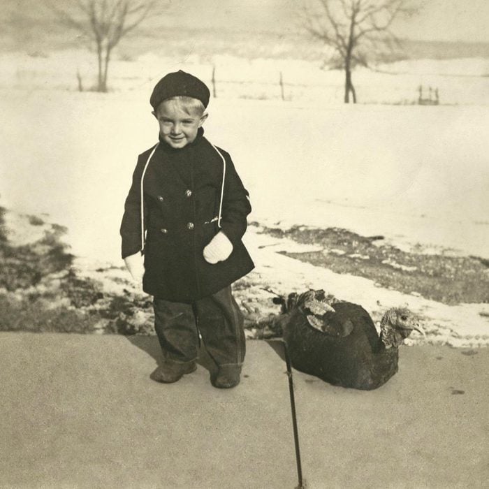 little boy froom the 1930s standing on snowy sidewalk next to a turkey