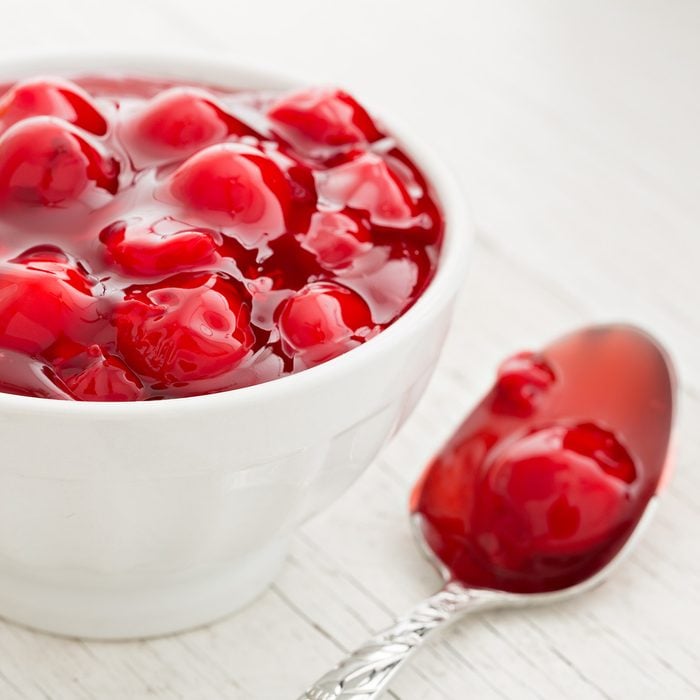 A high angle close up shot of a bowl full of cherry pie filling and a spoon.