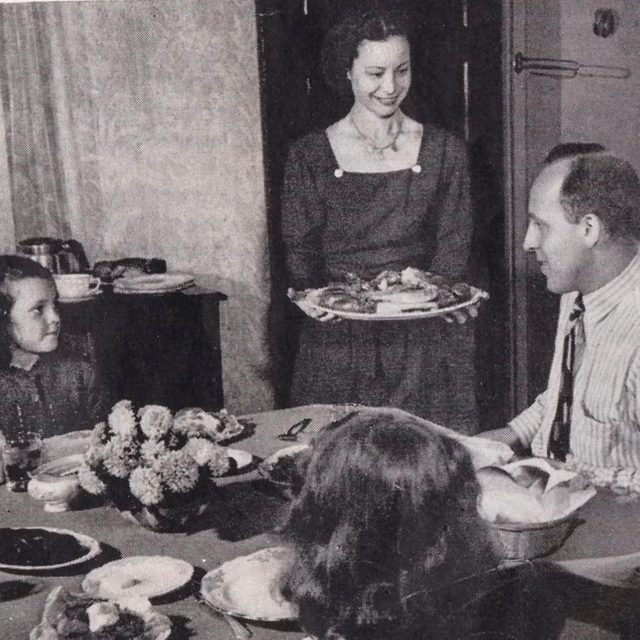 mother brings out plate of turkey to her family at the dinner table 1940s