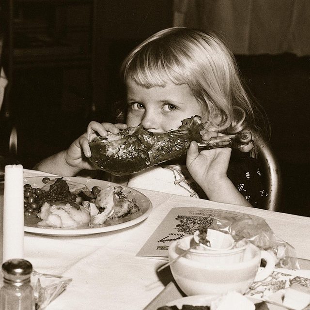 little girl looks into the camera as she takes bite out of turkey leg