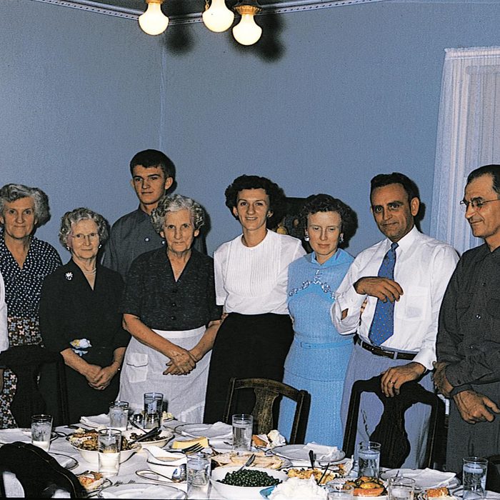 Multigenerational family stands behind thanksgiving dinner table to post for a photo