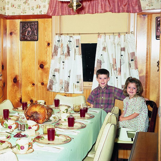 siblings sit at set dinner table in their retro 1960s kitchen