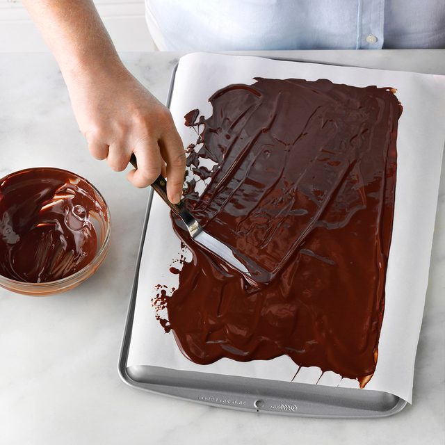 melted chocolate being spread on a cookie sheet into a thin layer