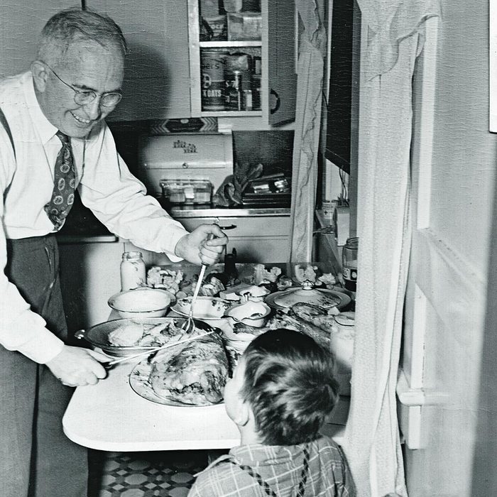 Older man carving tourkey while smiling at young boy 1930s