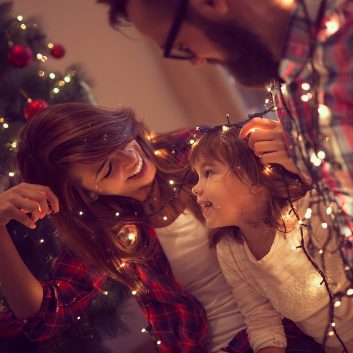 Beautiful young family enjoying their holiday time together, decorating Christmas tree, arranging the christmas lights and having fun