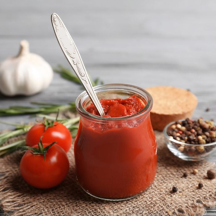 Delicious tomato paste in jar with ingredients on wooden background