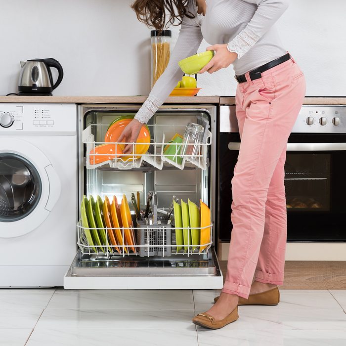 Woman unloading clean yellow dishes from dishwasher