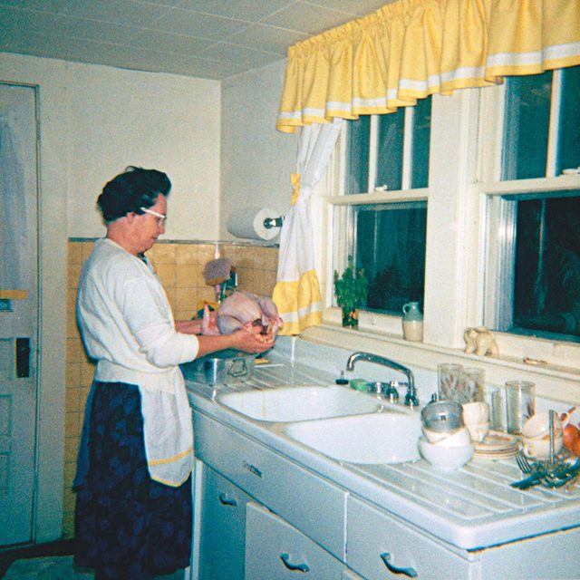 older woman holding raw turkey above sink 1960s