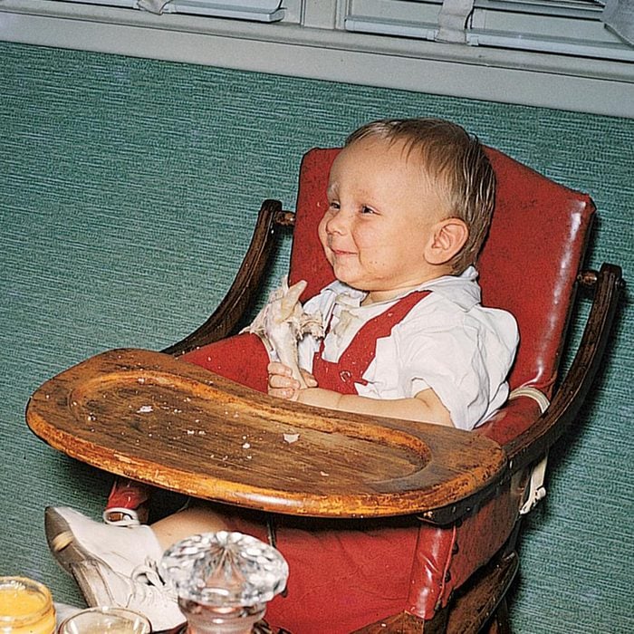 Infant boy smiles as he eats a turkey leg in his high chair on his first thanksgiving